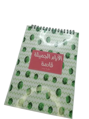 Couverture avant d'un carnet de notes à spirale avec un motif de pastèques vertes et un titre en arabe "Al-Ayam Al-Jamila Qadima" sur fond rose.