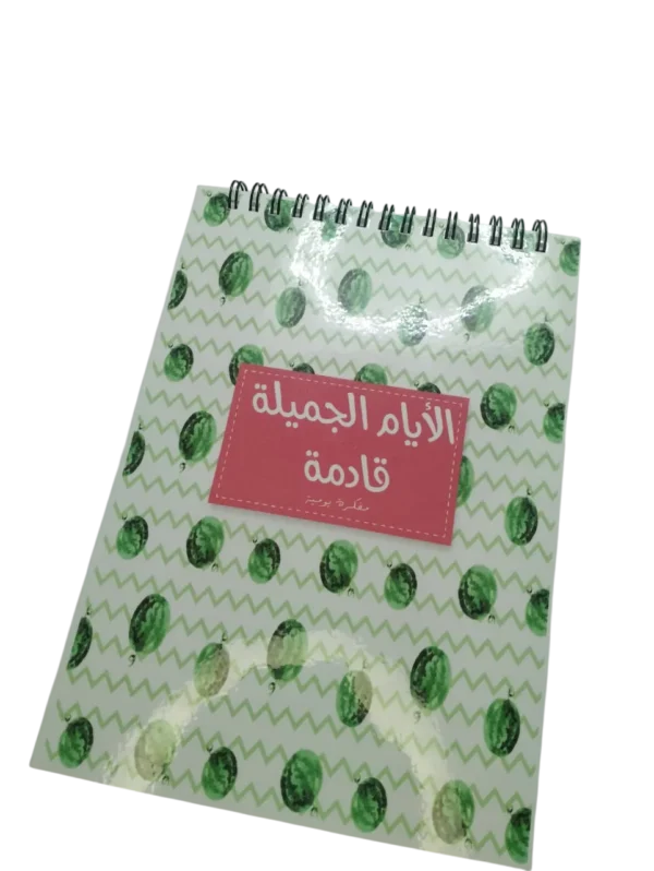 Couverture avant d'un carnet de notes à spirale avec un motif de pastèques vertes et un titre en arabe "Al-Ayam Al-Jamila Qadima" sur fond rose.