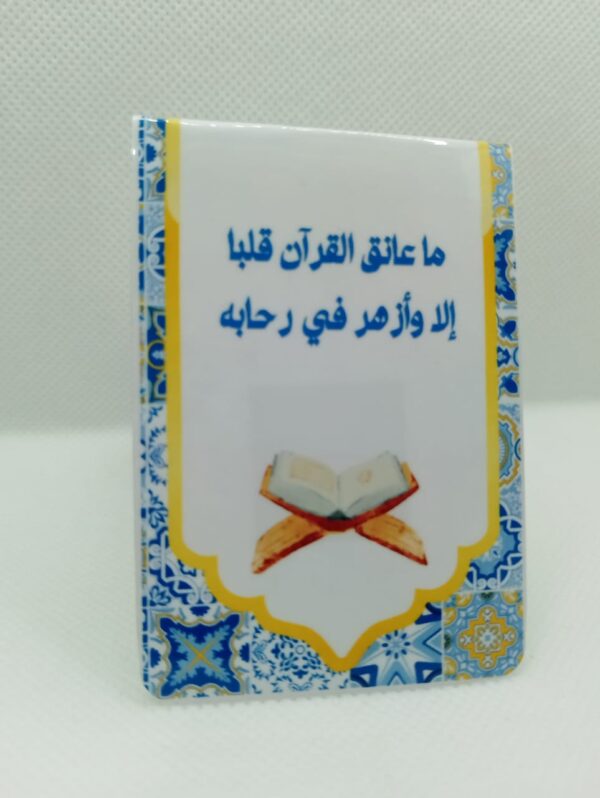 Marque-page magnétique debout affichant une citation sur le Coran en arabe ("Ma 'anaqa..."), illustration de livre ouvert et bordure motif mosaïque bleu et jaune.